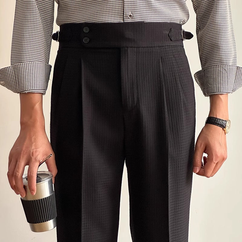 Mann in karierter Hemd und schwarzer Anzughose hält einen Kaffeebecher. Elegante Herrenmode, Business-Look, stilvolle Accessoires.