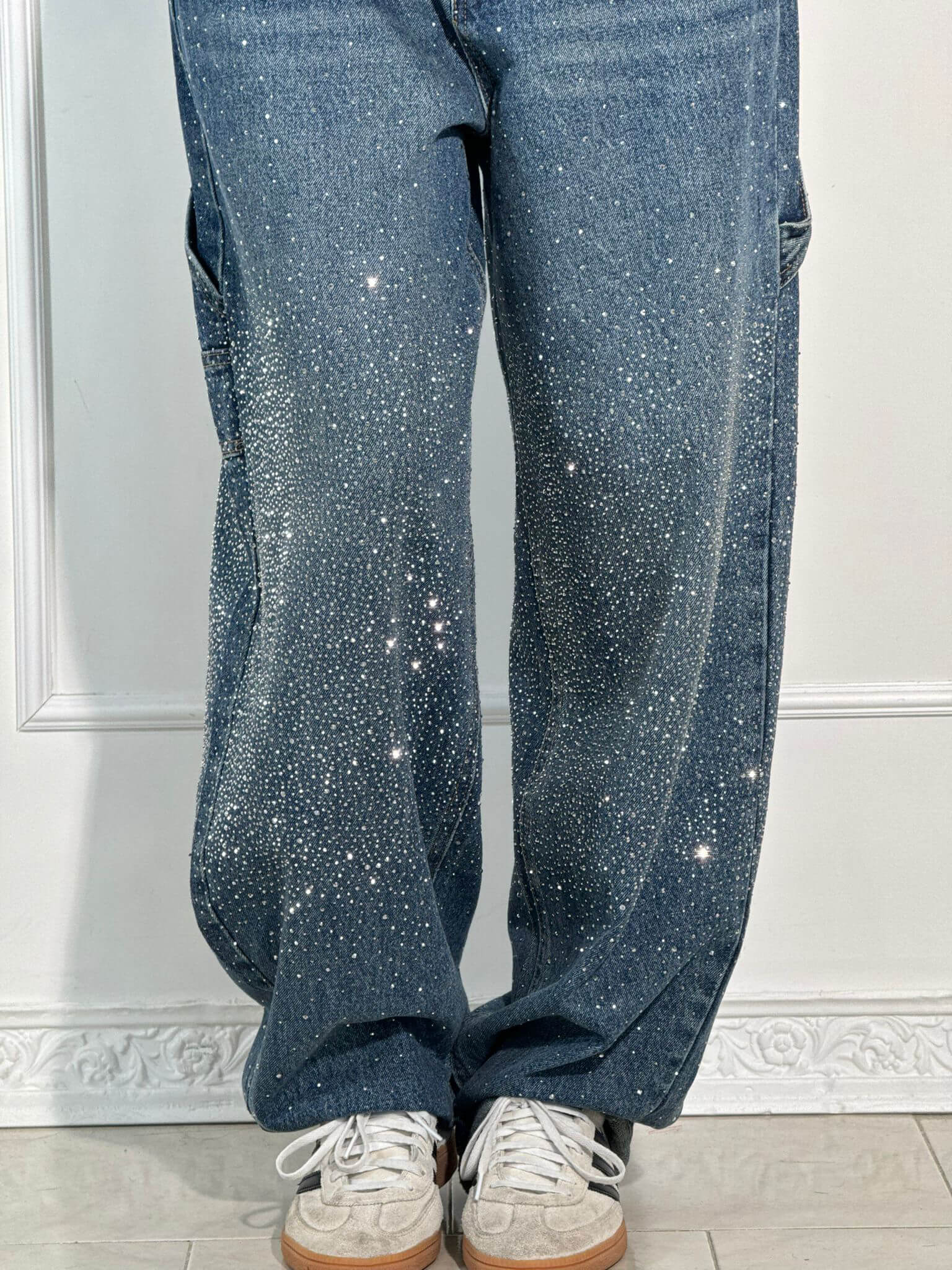 Jeans mit funkelnden Strasssteinen, getragen mit weißen Sneakern. Modetrend, Glitzer-Jeans, lässiger Stil, auffällige Denim-Mode.