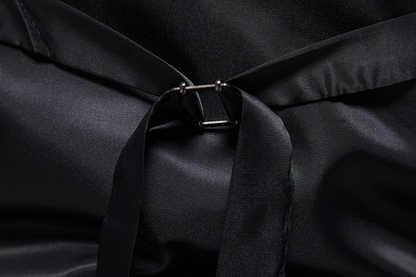 Schwarzes Satinkleid mit Schleife und Metallverschluss, elegante Abendmode, luxuriöser Stoff, Detailansicht, hochwertige Verarbeitung.