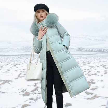Frau in mintgrünem Daunenmantel mit Fellkapuze, schwarzer Mütze und weißer Tasche steht im verschneiten Winterlandschaft. Wintermode, Outdoor-Bekleidung.