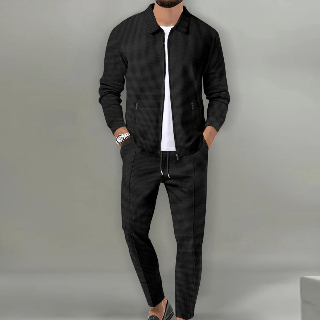 Mann in schwarzer Jacke und Hose, weißes T-Shirt, Armbanduhr, grauer Hintergrund. Modischer Herrenanzug, lässiger Stil, elegante Kleidung.