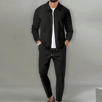 Mann in schwarzer Jacke und Hose, weißes T-Shirt, Armbanduhr, grauer Hintergrund. Modischer Herrenanzug, lässiger Stil, elegante Kleidung.