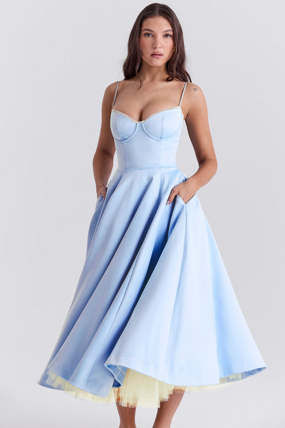 Frau in hellblauem, schulterfreiem Cocktailkleid mit weitem Rock und Spaghettiträgern, posiert vor grauem Hintergrund. Elegante Abendmode.