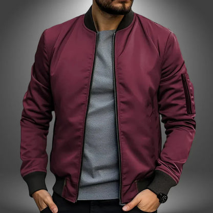 Mann in bordeauxroter Bomberjacke, grauem T-Shirt, schwarzer Hose. Modetrend, Herrenbekleidung, stilvolle Jacke, Freizeitlook.