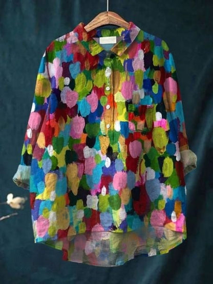 Bunte, abstrakt gemusterte Bluse auf einem Kleiderbügel vor dunklem Hintergrund. Farbenfrohes Design, langärmlig, Knopfleiste, Hemdkragen.