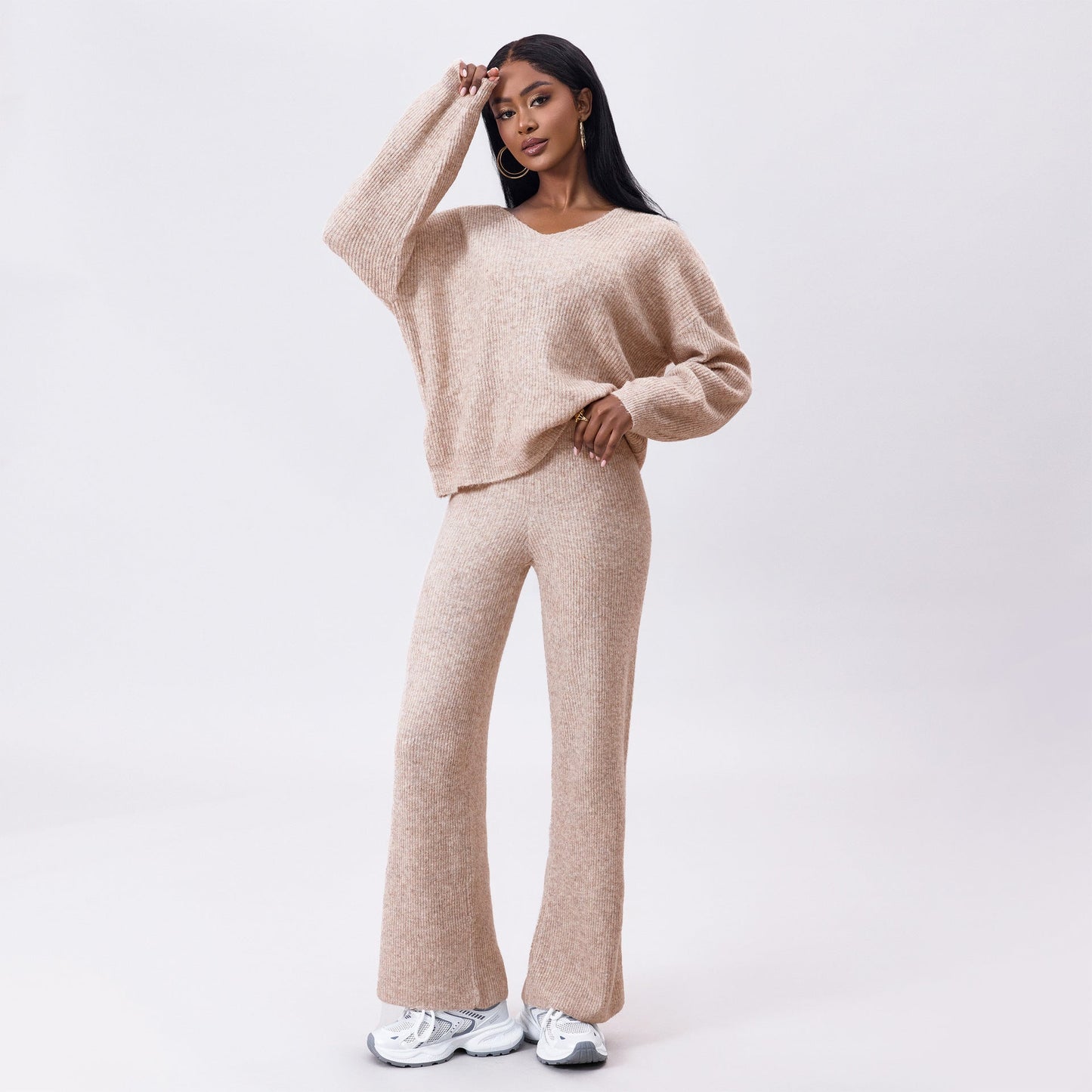 Frau in beigem Strickset mit Pullover und Hose, posiert vor weißem Hintergrund. Modetrend, gemütlicher Look, Herbstmode, Damenbekleidung.