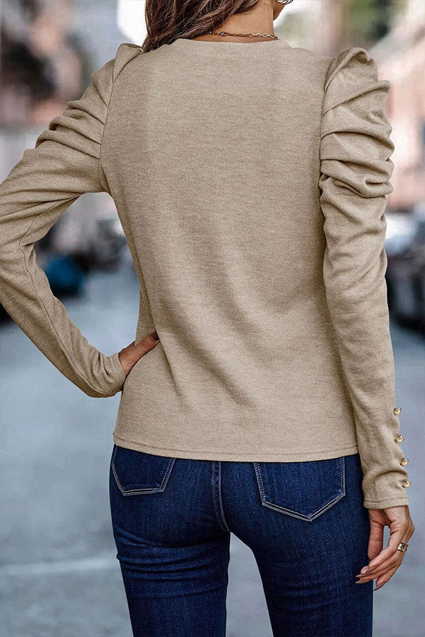 Frau in beigem Langarmshirt mit Rüschenärmeln und blauen Jeans, Rückansicht. Modetrend, Damenbekleidung, urbaner Stil.