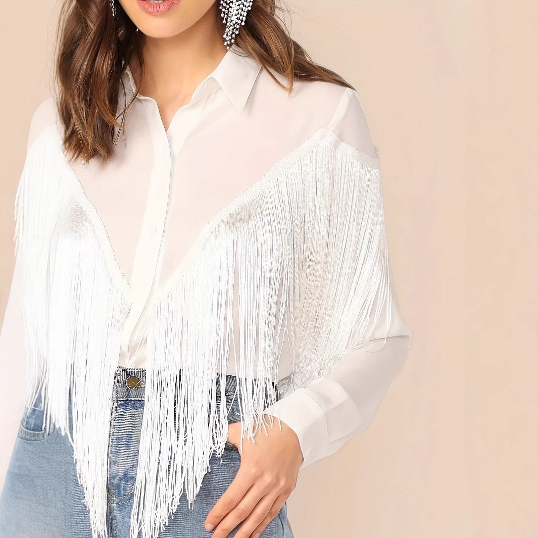 Frau trägt weiße Fransenbluse und blaue Jeans, modisches Outfit, eleganter Stil, trendige Damenmode, auffällige Ohrringe, moderne Kleidung.