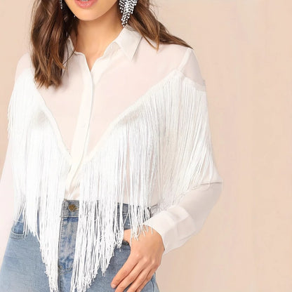 Frau trägt weiße Fransenbluse und blaue Jeans, modisches Outfit, eleganter Stil, trendige Damenmode, auffällige Ohrringe, moderne Kleidung.