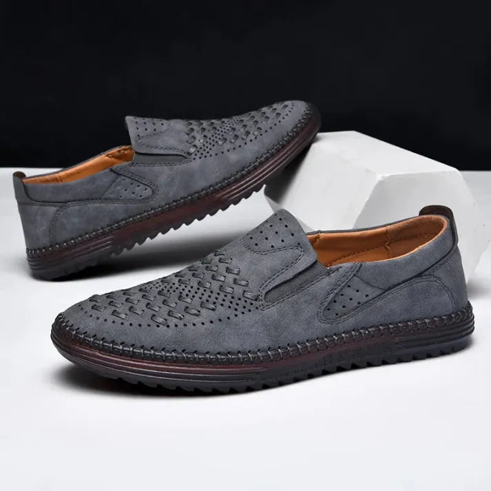 Graue Herren-Slipper aus Leder mit perforiertem Design, rutschfester Sohle und elegantem Look. Ideal für Freizeit und Business.