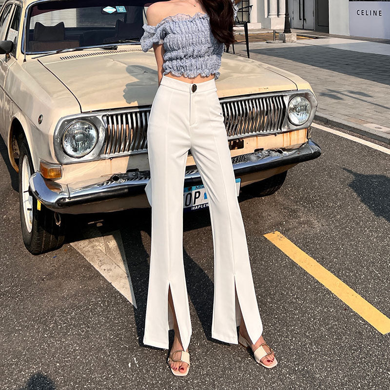 Frau in modischer Kleidung vor Vintage-Auto, trägt graues schulterfreies Top und weiße Schlaghose. Straßenmode, Retro-Auto, urbaner Stil.