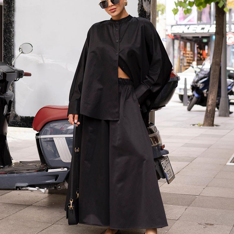 Frau in schwarzem, oversized Outfit mit Hemd und Rock, steht neben einem Motorrad auf einer städtischen Straße. Modetrend, Streetstyle, urbane Mode.