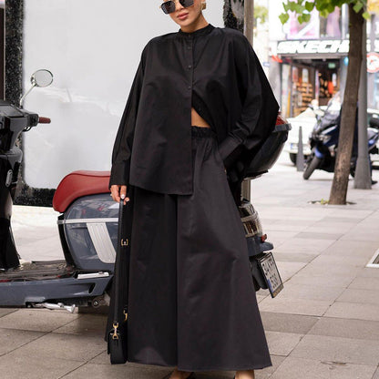 Frau in schwarzem, oversized Outfit mit Hemd und Rock, steht neben einem Motorrad auf einer städtischen Straße. Modetrend, Streetstyle, urbane Mode.