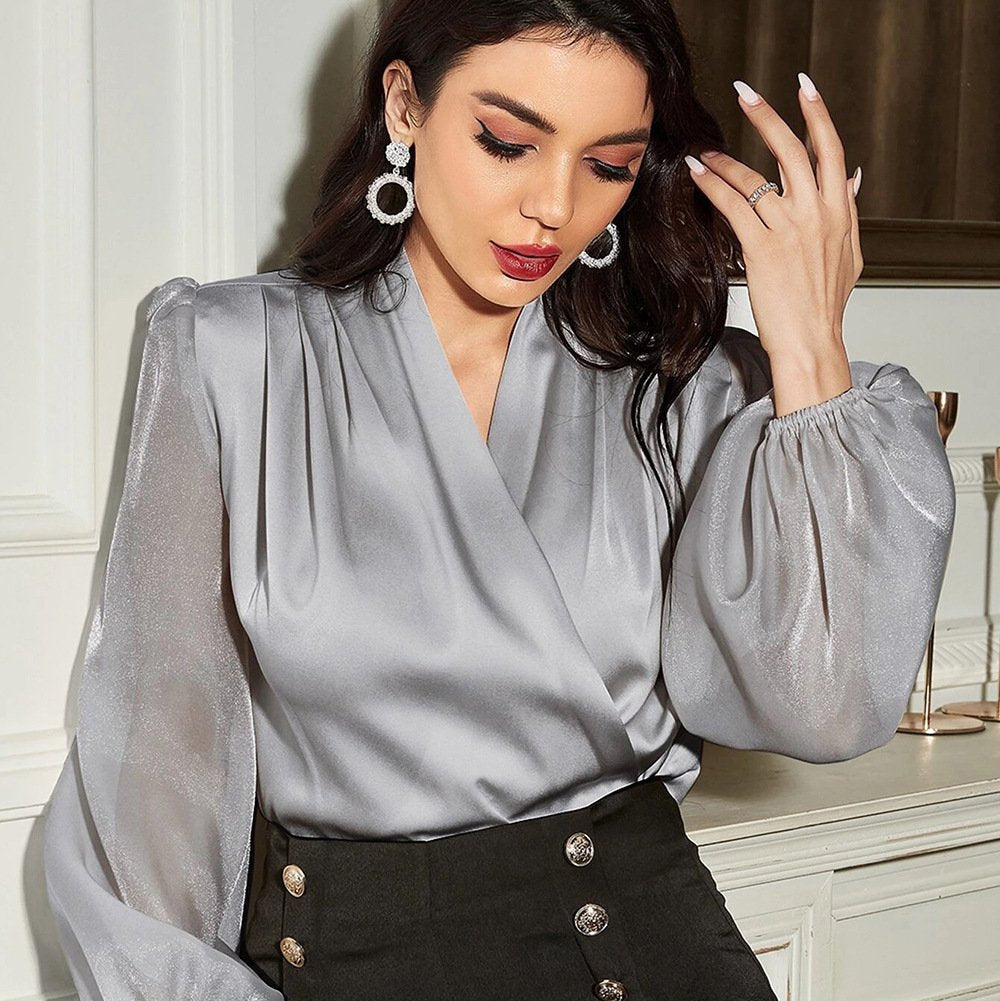 Frau in eleganter, silberner Satinbluse mit Puffärmeln und schwarzen Knöpfen, trägt auffällige Ohrringe und roten Lippenstift, stilvoll und modern.