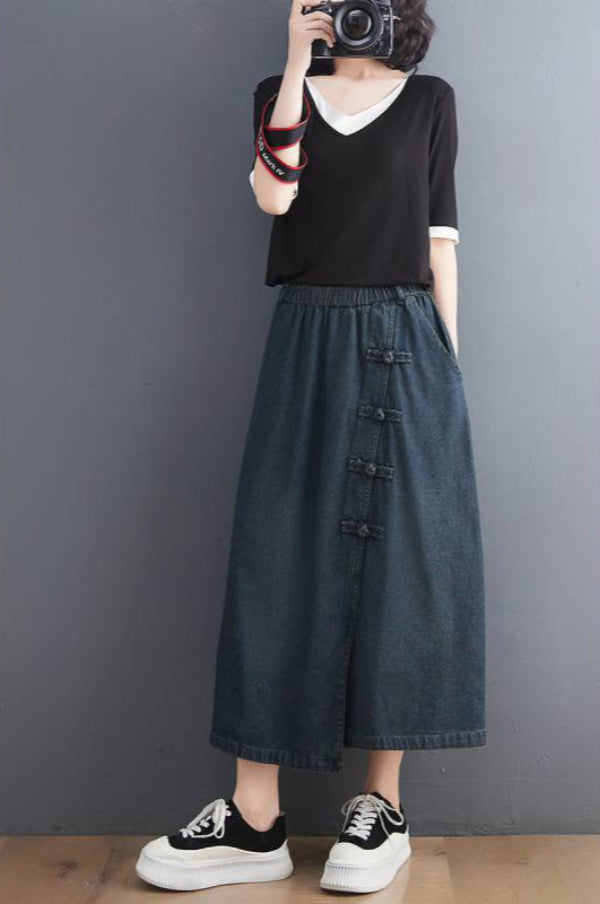 Frau in schwarzem T-Shirt und langer Jeansrock mit Knöpfen, trägt schwarz-weiße Sneaker, fotografiert sich selbst. Modetrend, lässiger Stil.