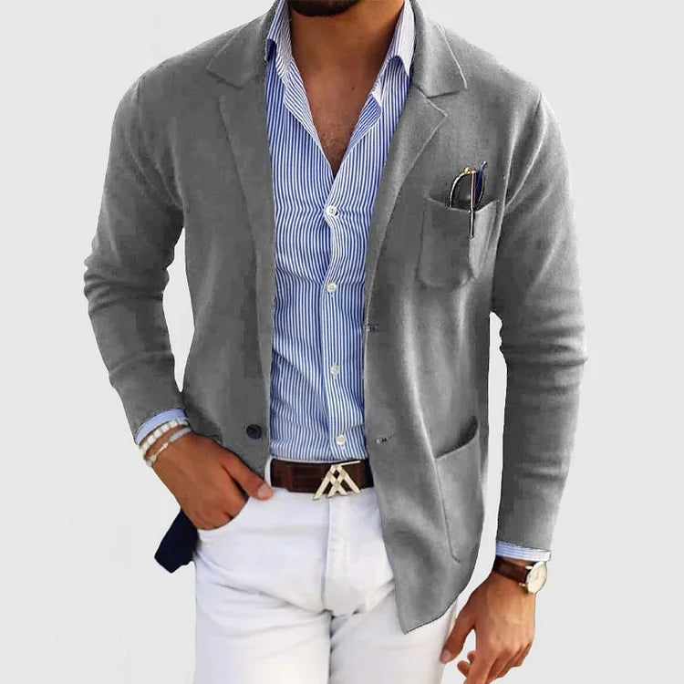 Mann in grauem Blazer und blau-weiß gestreiftem Hemd, weiße Hose, Armbänder und Uhr. Elegante Herrenmode, stilvoller Business-Look.