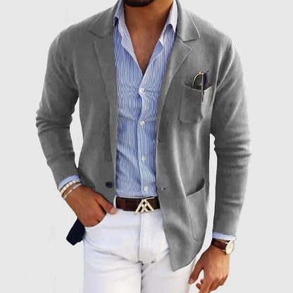 Mann in grauem Blazer und blau-weiß gestreiftem Hemd, weiße Hose, Armbänder und Uhr. Elegante Herrenmode, stilvoller Business-Look.