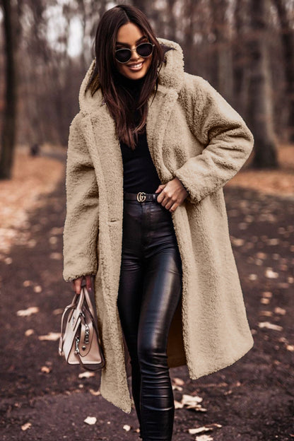 Frau im beigen Teddy-Mantel, schwarze Lederhose, Sonnenbrille, hält Handtasche, Herbstwald im Hintergrund. Modetrend, Herbstmode, stilvoll gekleidet.
