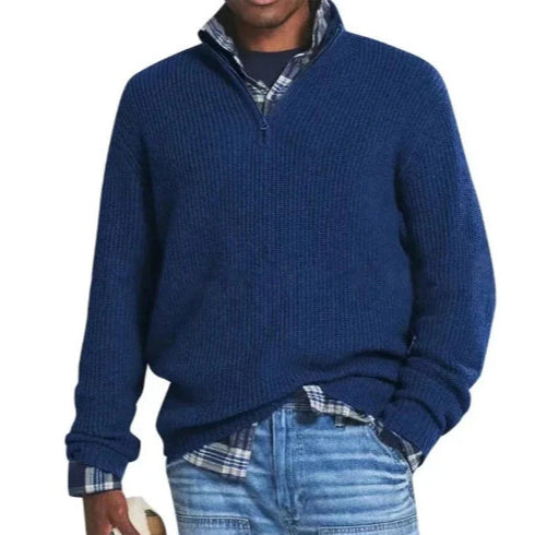 Blauer Herrenpullover mit Reißverschluss, getragen über kariertem Hemd und Jeans. Modischer Freizeitlook für Herbst und Winter.
