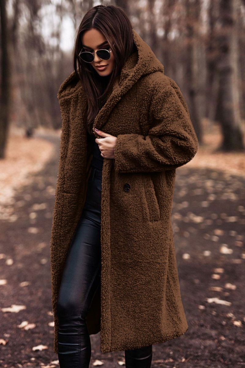Frau im braunen Teddy-Mantel und Sonnenbrille spaziert im herbstlichen Wald. Modetrend, Herbstmode, stilvoller Look, Outdoor-Kleidung.