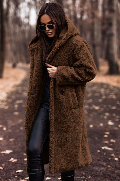 Frau im braunen Teddy-Mantel und Sonnenbrille spaziert im herbstlichen Wald. Modetrend, Herbstmode, stilvoller Look, Outdoor-Kleidung.