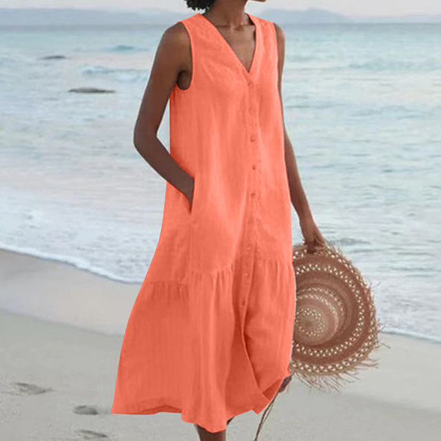 Frau in orangefarbenem Sommerkleid am Strand, hält Strohhut. Perfektes Outfit für Strandurlaub, Sommermode, lässiger Stil.