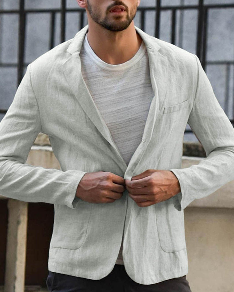 Mann in grauem Leinenblazer und T-Shirt, steht vor einem Fenster. Elegante Herrenmode, lässiger Stil, ideal für Frühling und Sommer.