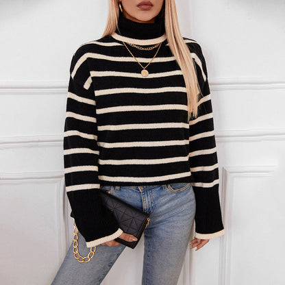 Frau in gestreiftem Pullover, blauer Jeans, hält schwarze Clutch mit goldener Kette. Modetrend, Herbstmode, eleganter Look.