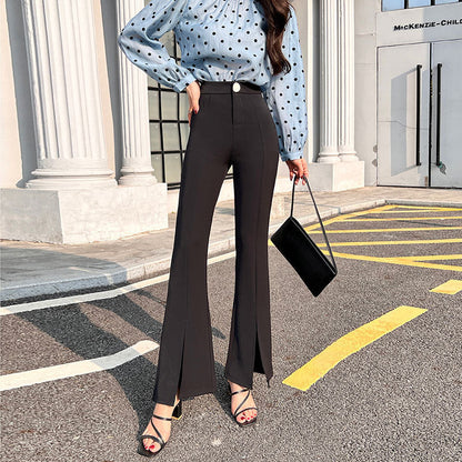 Frau in modischer schwarzer Schlaghose und gepunkteter Bluse, trägt schwarze Handtasche und Sandalen, steht auf Straße vor modernem Gebäude.