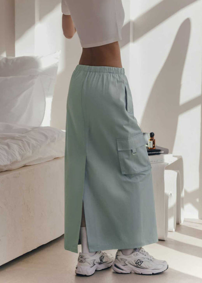 Frau in mintgrüner Cargo-Rock und weißen Sneakers steht in modernem Schlafzimmer. Mode, Streetwear, Trend, Damenbekleidung, Innenraum.