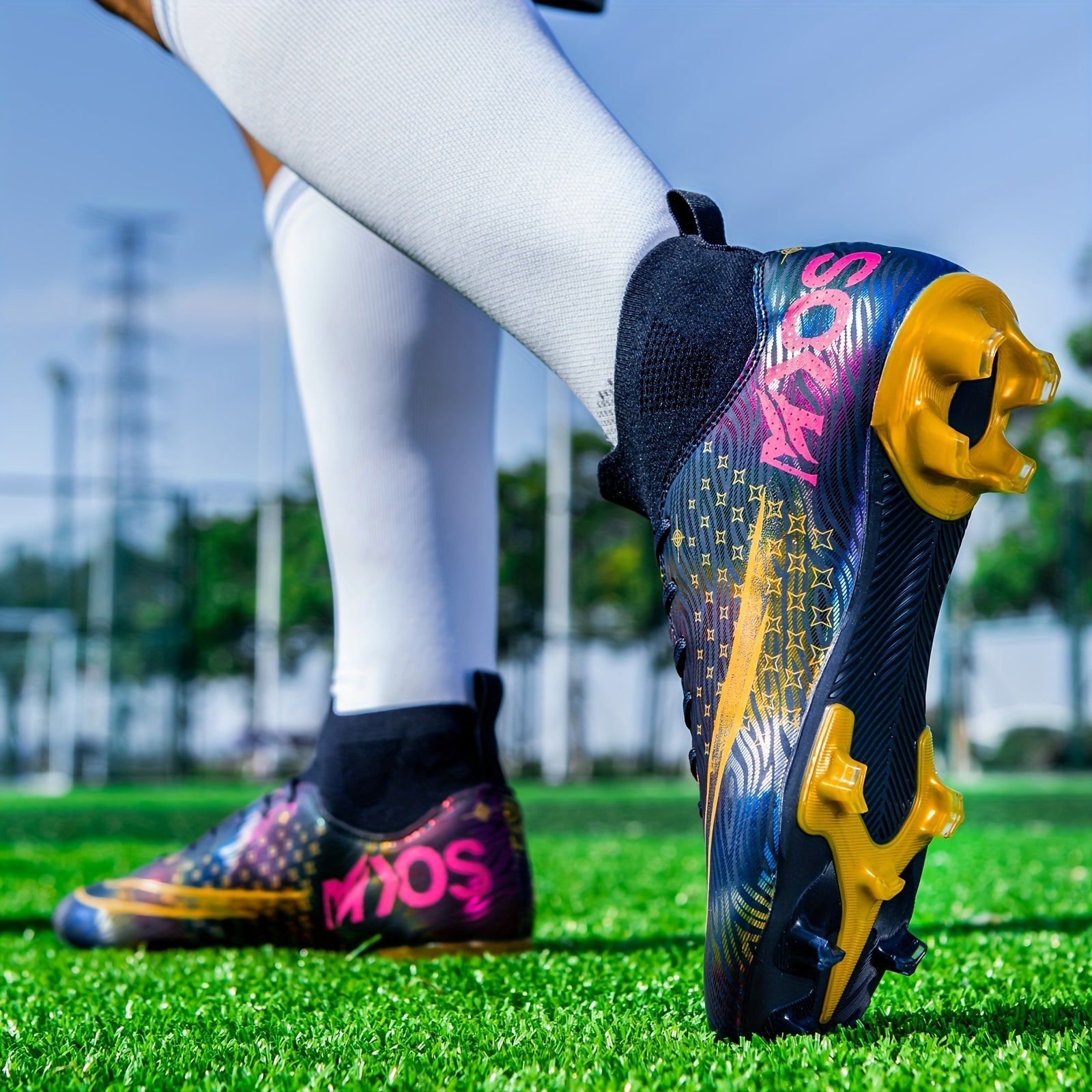 Fußballschuhe auf Rasenplatz, bunte Nike Mercurial mit goldenen Stollen, getragen von Spieler mit weißen Socken, im Hintergrund unscharfe Bäume.