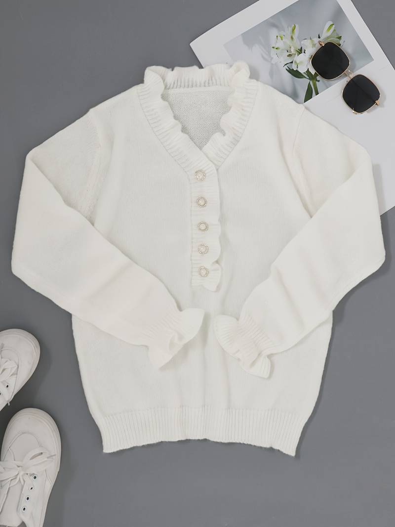 Weiße Strickjacke mit Rüschen und Perlenknöpfen auf grauem Hintergrund, neben weißen Sneakers und Sonnenbrille mit Blumenfoto.