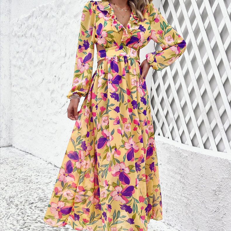 Frau in langem, gelbem Blumenkleid mit rosa und violetten Blumen, steht vor weißer Wand. Modetrend, Sommerkleid, florales Design.