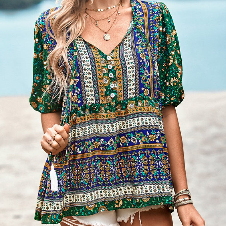 Frau trägt buntes Boho-Kleid mit Blumenmuster, V-Ausschnitt und kurzen Ärmeln am Strand. Sommermode, Boho-Stil, Damenbekleidung.