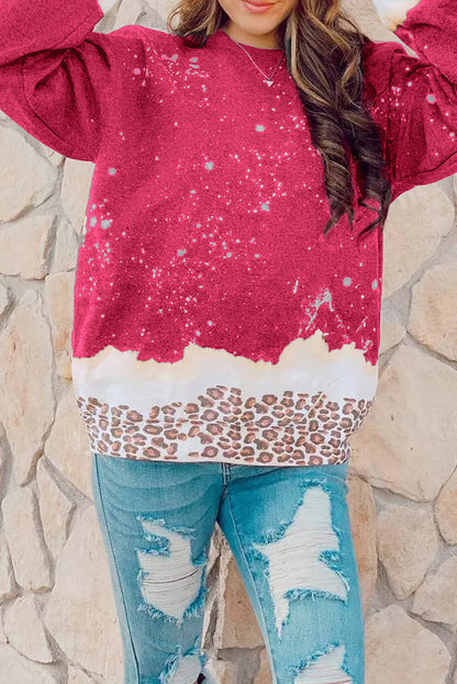 Frau in rotem Pullover mit Sternenmuster und Leoparden-Details, kombiniert mit zerrissenen Jeans vor einer Steinwand. Modetrend, lässiger Look.