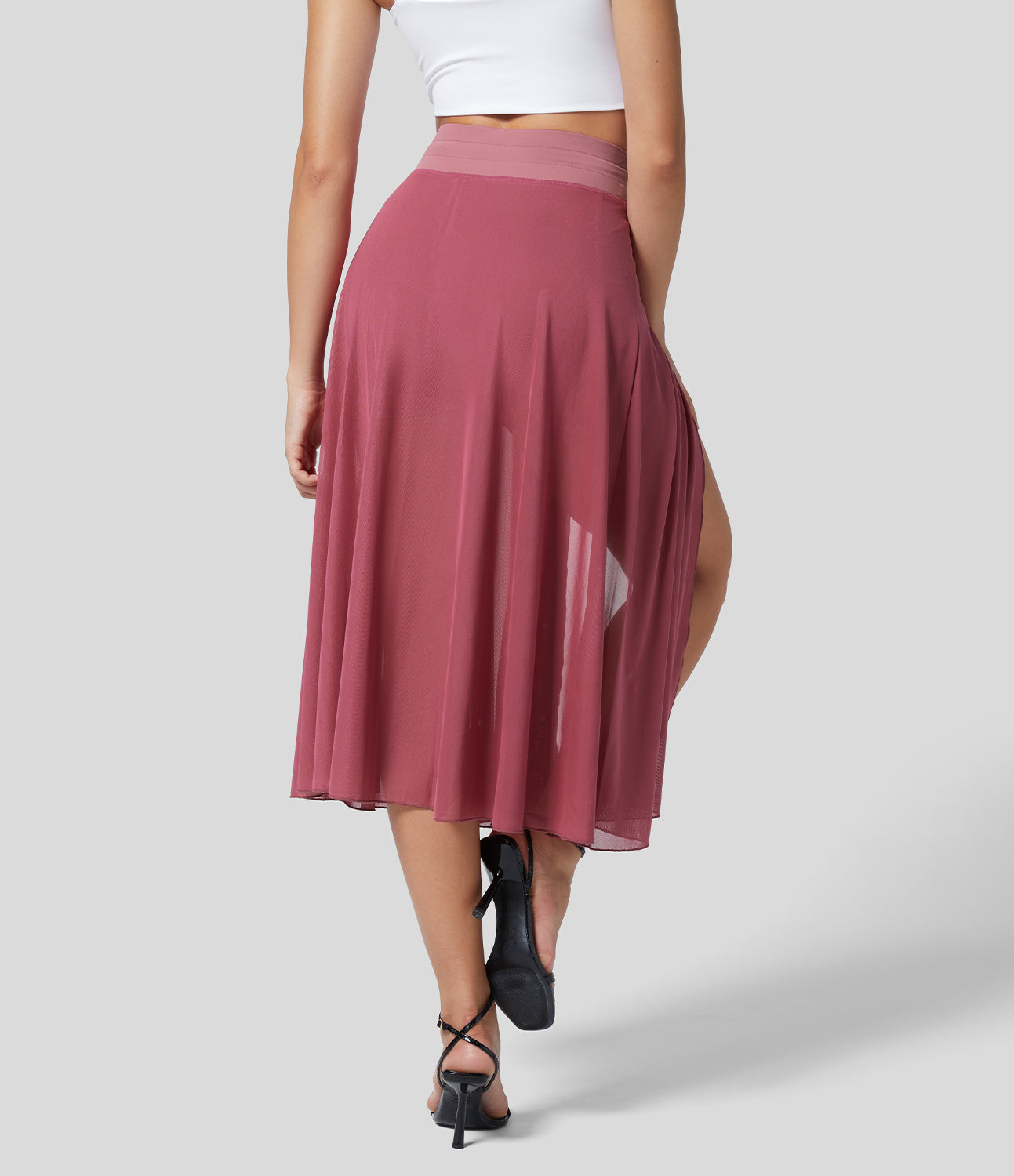 Frau in rosa, fließendem Midirock und weißem Top, Rückansicht. Modetrend, Sommeroutfit, eleganter Stil, Damenmode, bequeme Kleidung.
