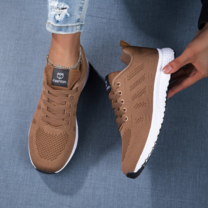 Braune Sportschuhe mit weißer Sohle, gestricktem Obermaterial und Markenlogo, getragen von Person in zerrissener Jeans auf blauem Hintergrund.