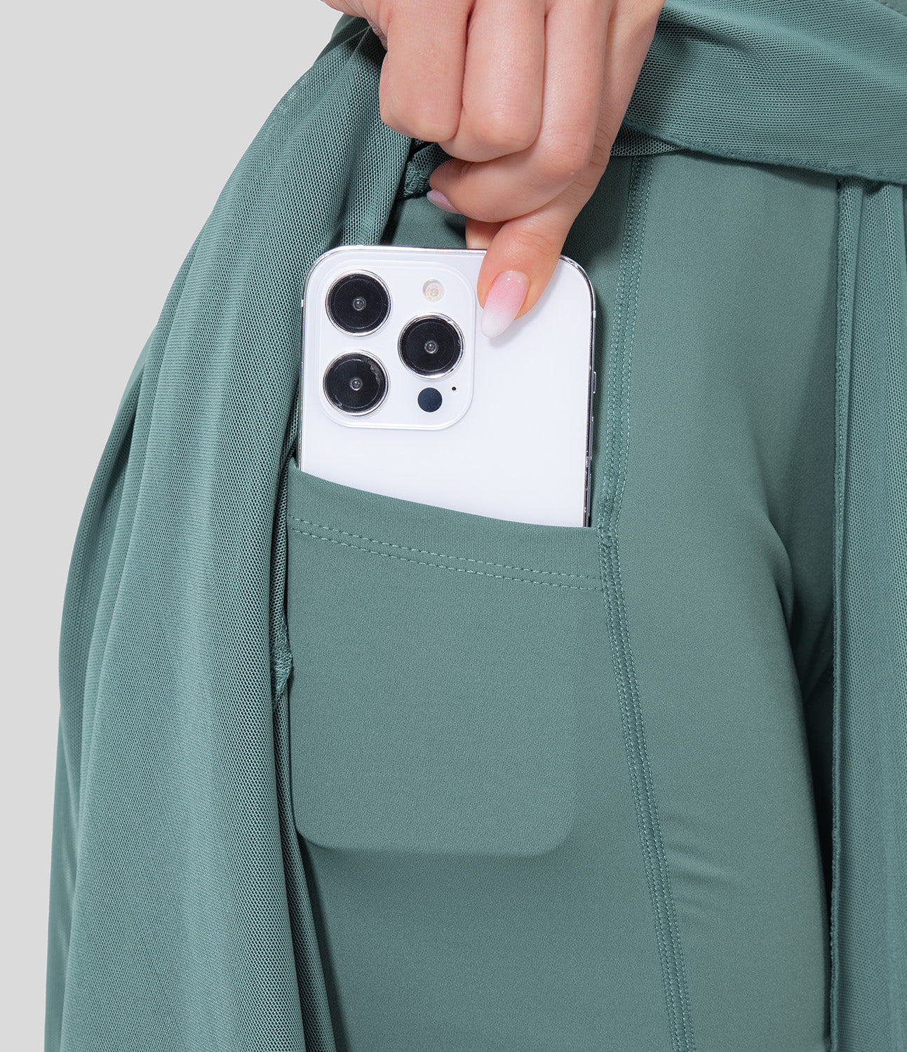 Hand hält ein weißes Smartphone mit drei Kameras in der Tasche einer grünen Sporthose. Moderne Technologie, Smartphone, Sportbekleidung.