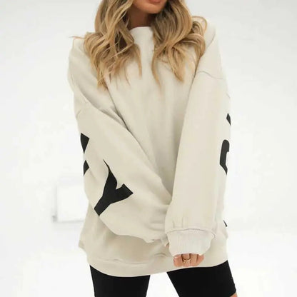 Dame in beigem Oversize-Pullover mit schwarzen Buchstaben, kombiniert mit schwarzen Leggings. Modetrend, lässiger Stil, Herbstmode.