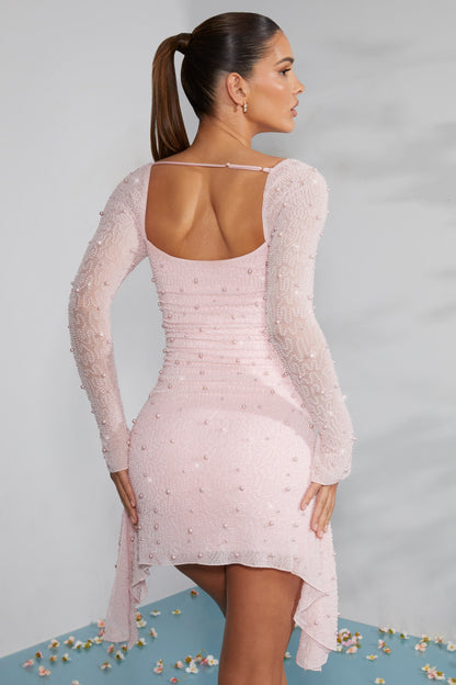 Frau in rosa, figurbetontem Kleid mit langen Ärmeln und Perlendetails, steht mit dem Rücken zur Kamera. Elegante Mode, Abendkleid, stilvoll.