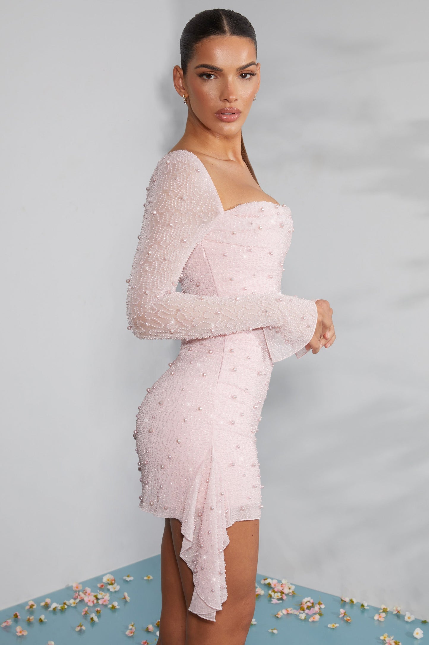 Elegantes rosa Kleid mit Perlen, asymmetrischem Saum und langen Ärmeln, getragen von einer Frau. Perfekt für Abendmode und besondere Anlässe.