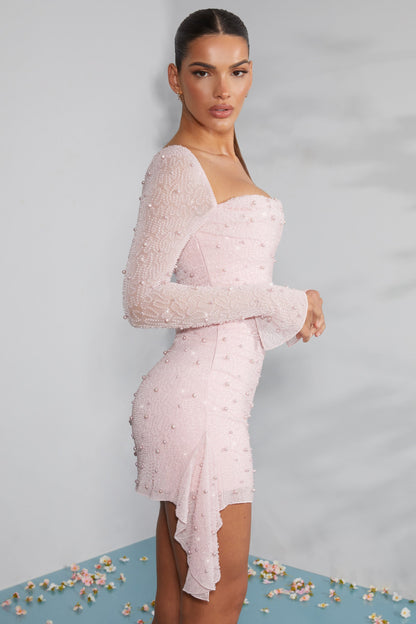 Elegantes rosa Kleid mit Perlen, asymmetrischem Saum und langen Ärmeln, getragen von einer Frau. Perfekt für Abendmode und besondere Anlässe.