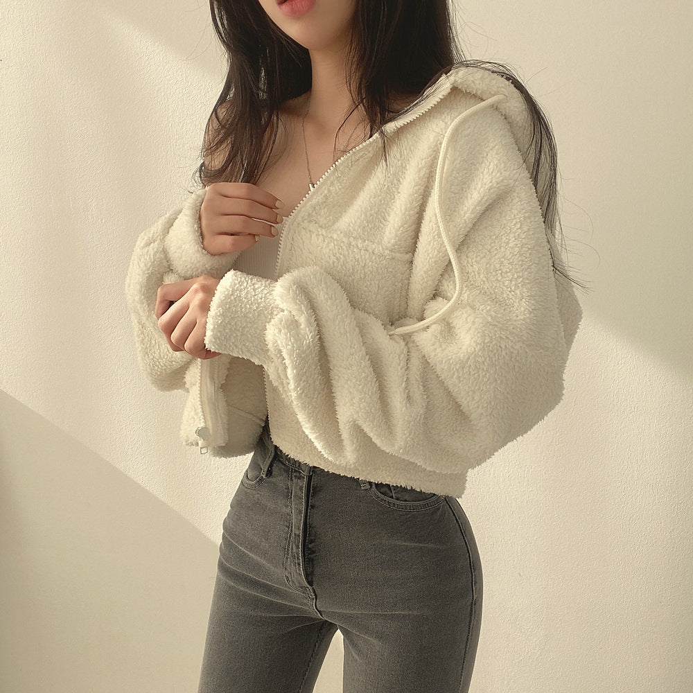 Frau in weißer Teddyjacke und grauer Jeans vor hellem Hintergrund. Modetrend, Wintermode, lässiger Stil, gemütliche Kleidung.