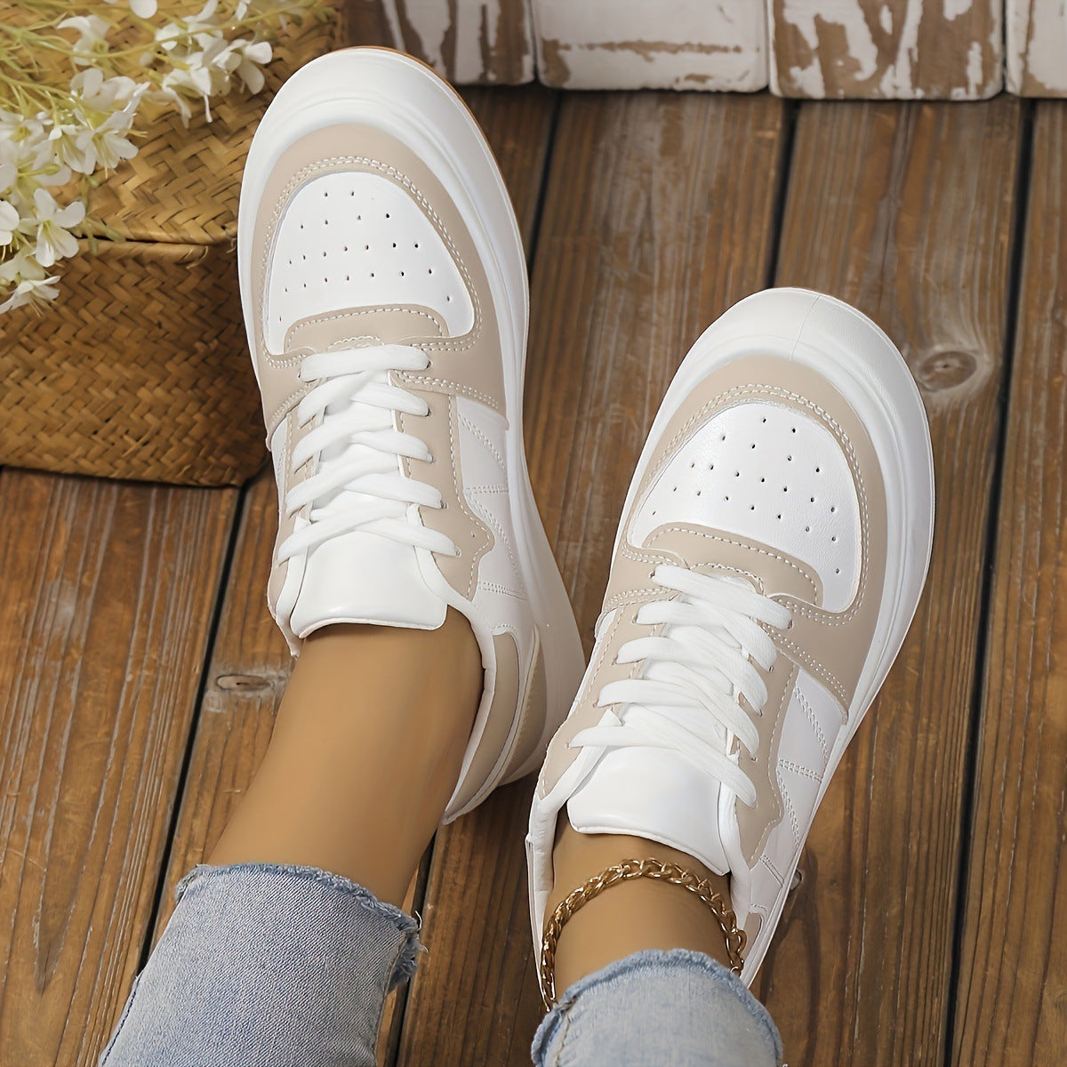 Beige-weiße Sneaker auf Holzboden, getragen von Person in blauen Jeans. Modische Damen-Schuhe, Freizeit-Look, trendige Sneaker für Alltag.