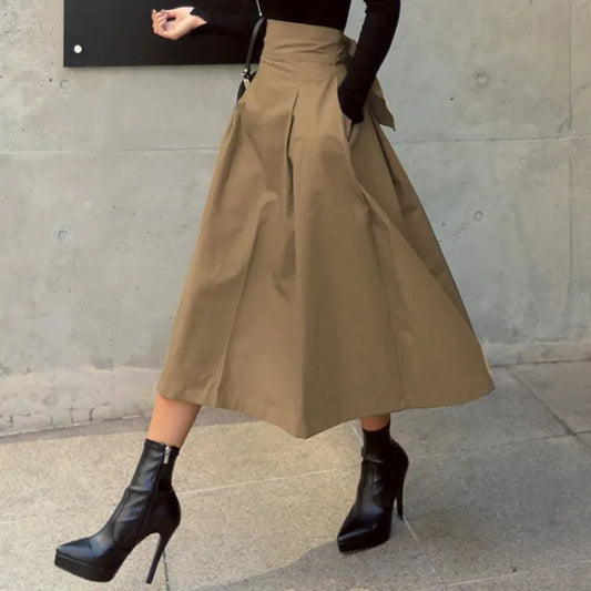Frau in braunem A-Linien-Rock und schwarzen Stiefeln mit hohen Absätzen, geht an Betonwand vorbei. Modetrend, eleganter Herbstlook.