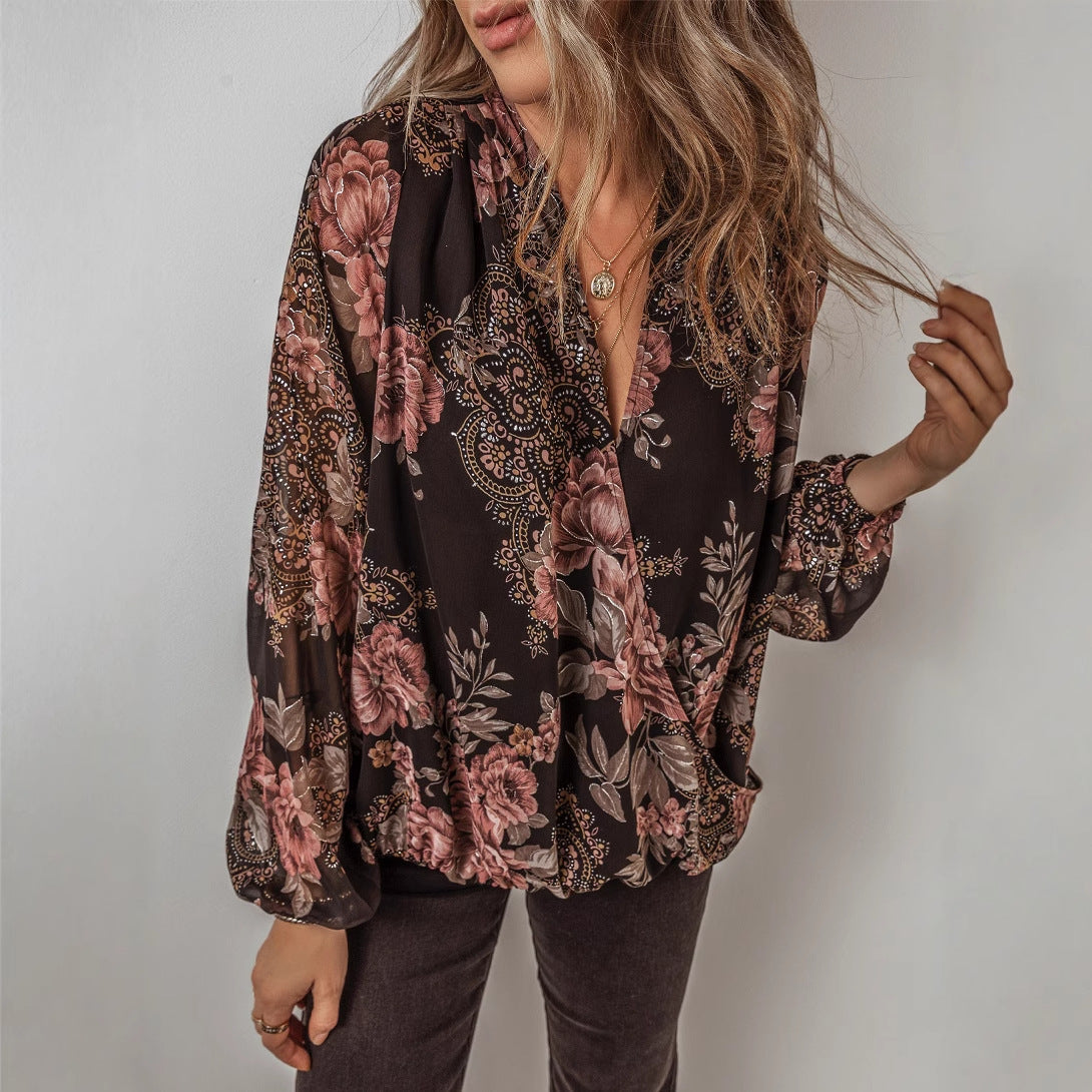 Frau trägt eine geblümte Bluse mit langen Ärmeln, kombiniert mit braunen Hosen. Modetrend, Damenmode, Herbstoutfit, florales Design.