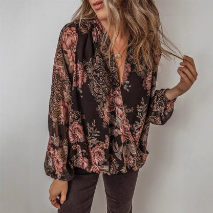 Frau trägt eine geblümte Bluse mit langen Ärmeln, kombiniert mit braunen Hosen. Modetrend, Damenmode, Herbstoutfit, florales Design.