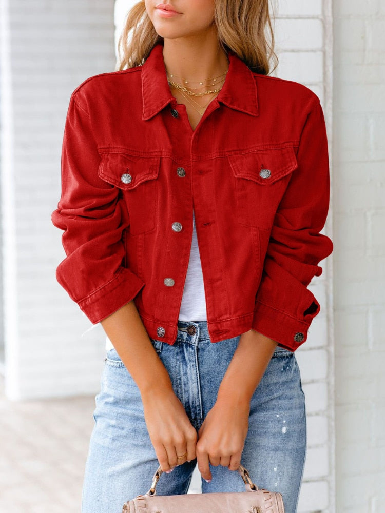 Frau in roter Jeansjacke, weißem T-Shirt und blauer Jeans vor weißer Wand. Modetrend, lässiger Stil, Damenmode, Streetwear.