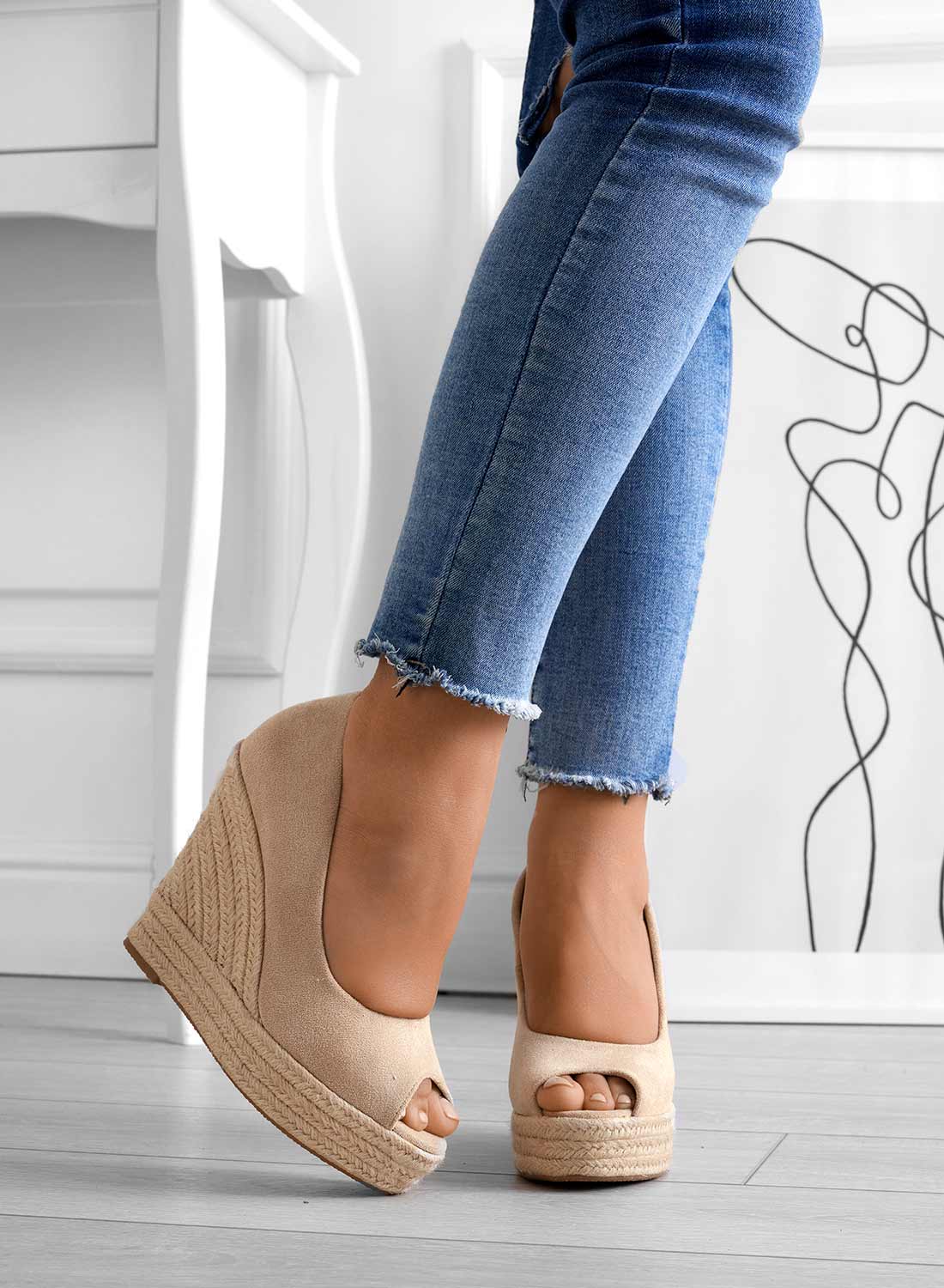 Frau trägt beige Keilabsatz-Sandalen mit offener Spitze, kombiniert mit blauen Jeans. Modetrend, Damenmode, Sommerschuhe, stilvolle Sandalen.
