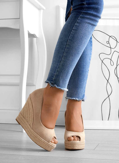 Frau trägt beige Keilabsatz-Sandalen mit offener Spitze, kombiniert mit blauen Jeans. Modetrend, Damenmode, Sommerschuhe, stilvolle Sandalen.